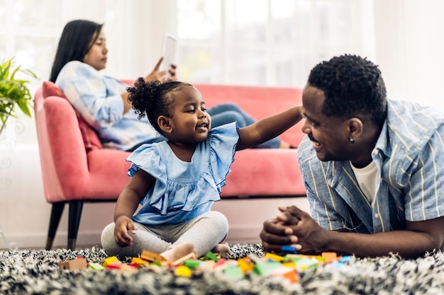 Retrato de amor feliz família negra pai e mãe afro-americanos com atividade sorridente de garotinha aprender e treinar habilidade do cérebro jogar com brinquedo construir blocos de madeira jogo de educação em casa