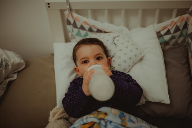 Foto retrato de ângulo alto de menino e menina bonitos bebendo leite enquanto estão deitados na cama