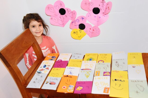 Foto retrato de ângulo alto de uma menina bonita e sorridente com cartões de saudação coloridos na mesa em casa