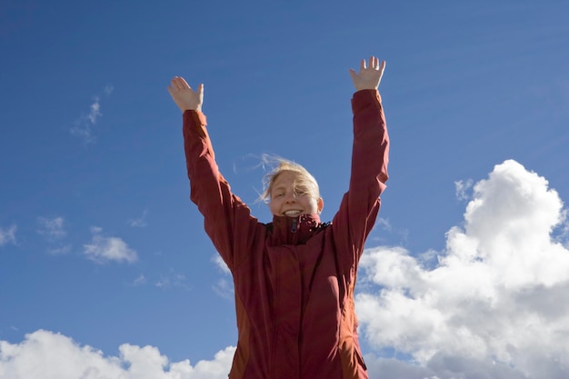Foto retrato de ângulo baixo de mulher madura com os braços levantados de pé contra o céu durante o dia ensolarado