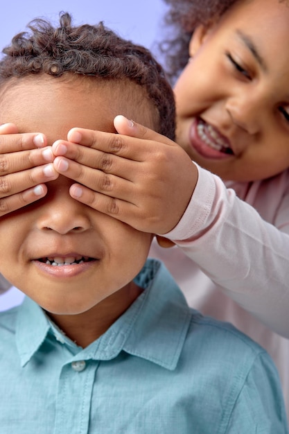 Retrato de animada alegre despreocupada menina e menino cobrindo os olhos com os braços um para o outro e menino sorrindo sinceramente, rindo, se divertindo e jogando peek a boo jogo. tiro de estúdio interno