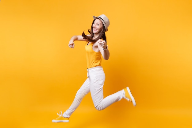 Retrato de animado sorridente jovem feliz pulando alta mulher com chapéu de palha de verão, copie o espaço isolado em fundo amarelo laranja. Emoções sinceras de pessoas, conceito de estilo de vida de paixão. Área de publicidade.