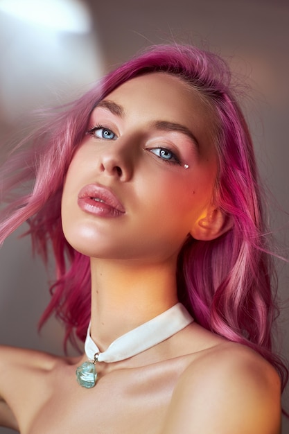 Retrato de arte beleza de uma mulher com cabelo rosa, coloração criativa. Destaques coloridos brilhantes e sombras no rosto, uma garota com jóias. Cabelos tingidos ao vento