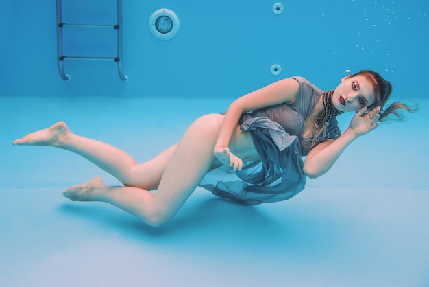 retrato de arte surreal de jovem de vestido cinza e cachecol frisado debaixo d'água na piscina