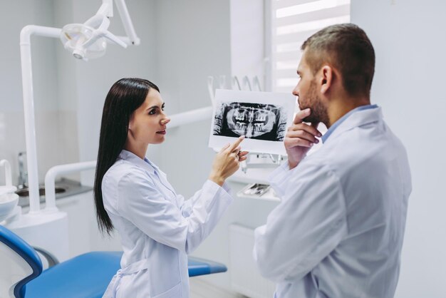 Retrato de assistente feminina falando com um médico pensativo segurando no raio-x na clínica moderna