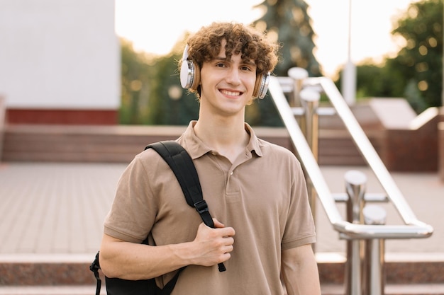 Retrato de atraente estudante masculino de cabelos encaracolados em fones de ouvido sorrindo