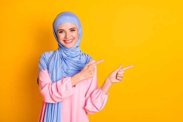 Retrato de atraente muslimah alegre usando hijab, demonstrando o anúncio do espaço de cópia isolado em um fundo de cor amarela brilhante