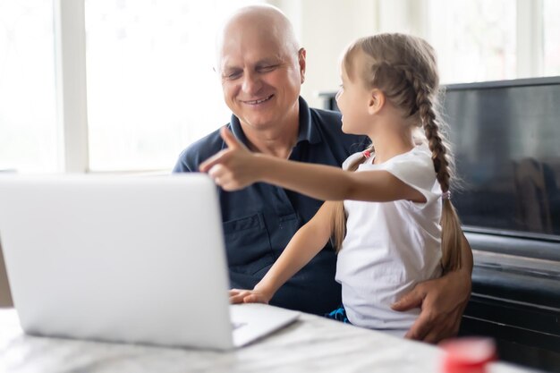 Retrato de avô e neta fazendo lição de casa com o laptop.