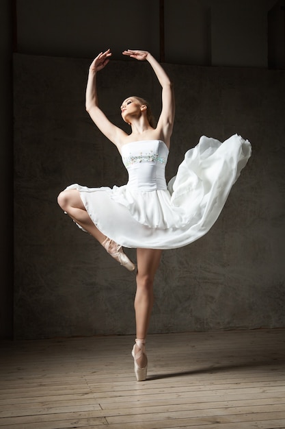 Foto retrato de bailarina profissional vestida de branco se apresentando em estúdio com os braços para cima