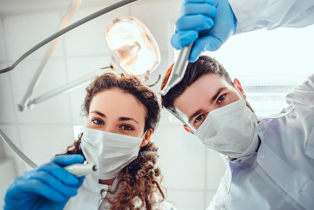 Retrato de baixo ângulo de dentistas masculinos e femininos usando máscaras na clínica odontológica