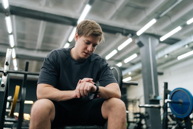 Foto retrato de baixo ângulo de um homem de fitness verificando o tempo de treino em um ginásio moderno olhando para um relógio com