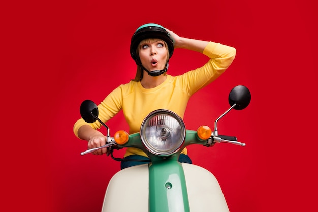 Retrato de baixo ângulo de uma garota alegre e alegre dirigindo uma motocicleta com rosto chocado