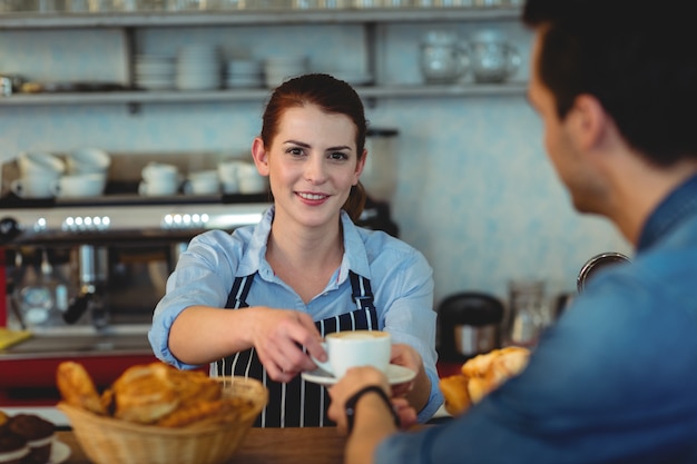 Retrato de barista confiante dando café ao cliente no café