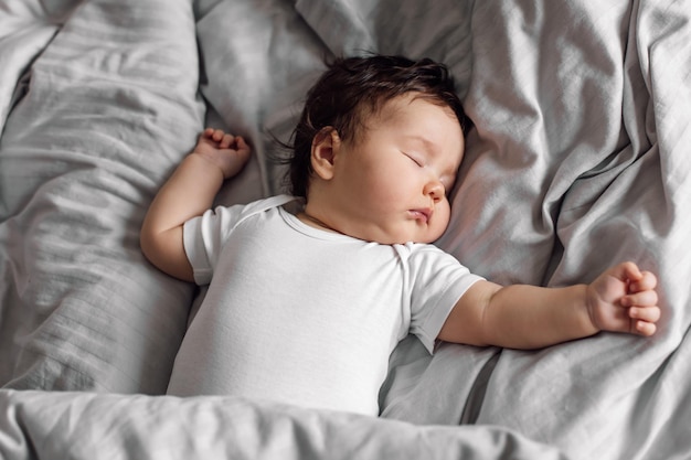 Retrato de bebê em roupa de dormir, deitado sob o cobertor cinza na cama em casa, dormindo nas costas, criança infantil no quarto, veja um doce sonho, espaço de cópia livre de fundo cinza Cuidados infantis e conceito de sono saudável