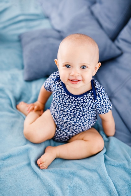 Retrato de bebê feliz rindo com olhos azuis, camisa azul, sentado no sofá.