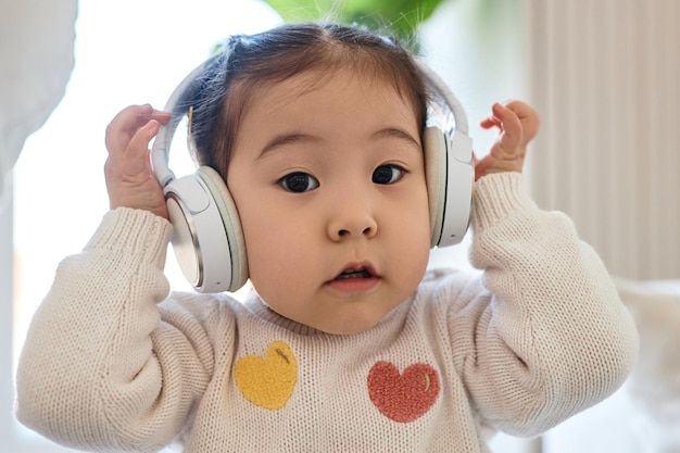 Retrato de bebê fofo asiático em fones de ouvido sem fio, olhando para a câmera enquanto ouve música