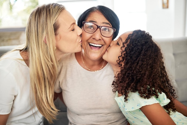 Retrato de beijo de família interracial e casa com vínculo amoroso e cuidado dos pais com avó, mãe e filho Sorriso feliz e sala de estar com crianças e apoio juntos, relaxar com os avós