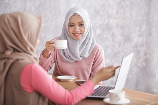 Retrato de belas mulheres muçulmanas explicando o projeto no laptop para seu irmão na cafeteria