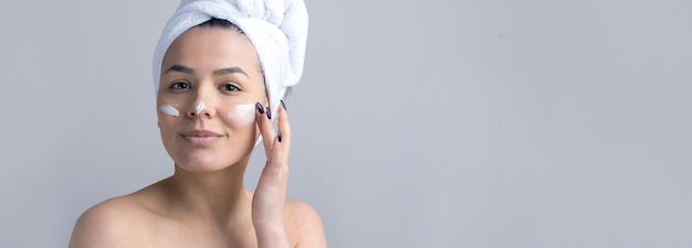 Retrato de beleza de mulher em toalha branca na cabeça aplica creme no rosto Skincare limpeza eco spa cosmético orgânico conceito relax