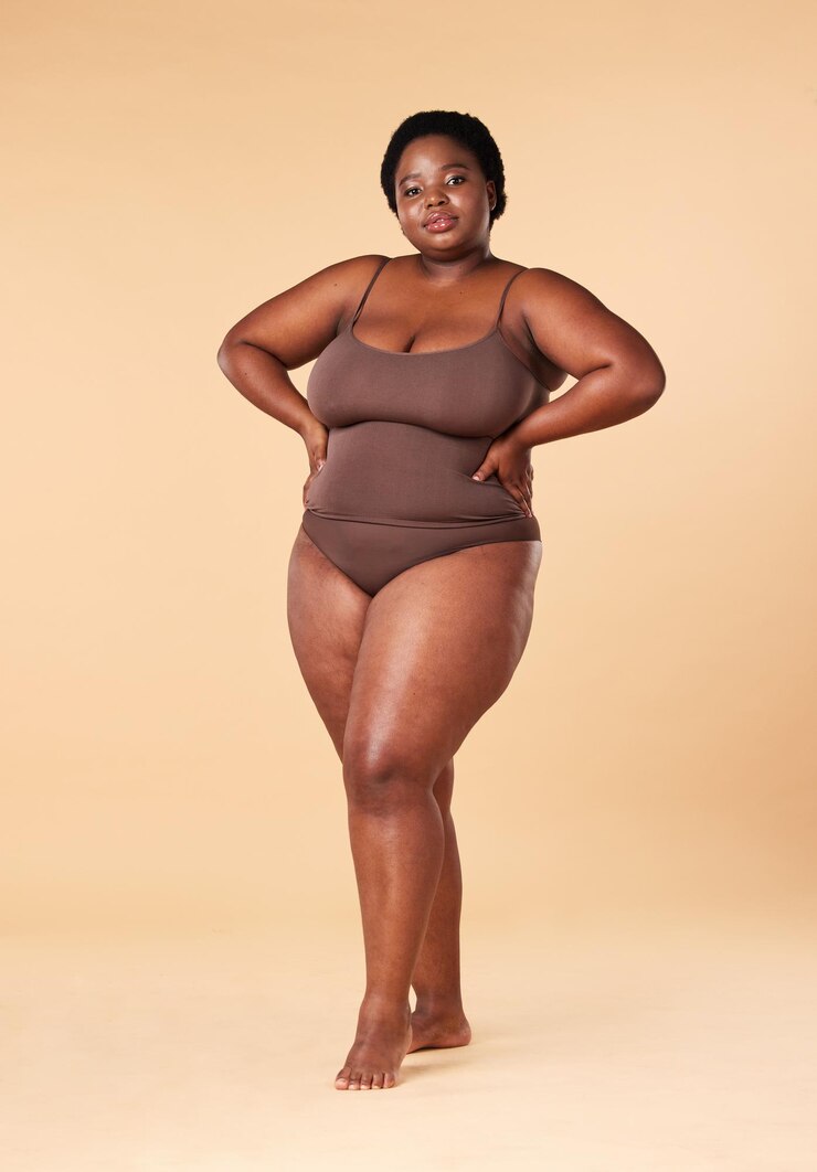 Foto retrato de bem-estar e tamanho grande com uma mulher negra modelo posando as mãos nos quadris no estúdio em um fundo bege cueca de beleza e natural com uma mulher sentada em um banquinho para positividade do corpo