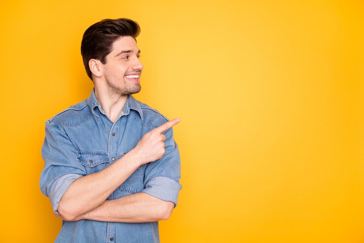 Retrato de bom conteúdo atraente alegre alegre cara apontando o dedo indicador ao lado anúncio copiar vazio preto lugar espaço seguir assinar isolado sobre brilhante vívido brilho vibrante parede cor amarela