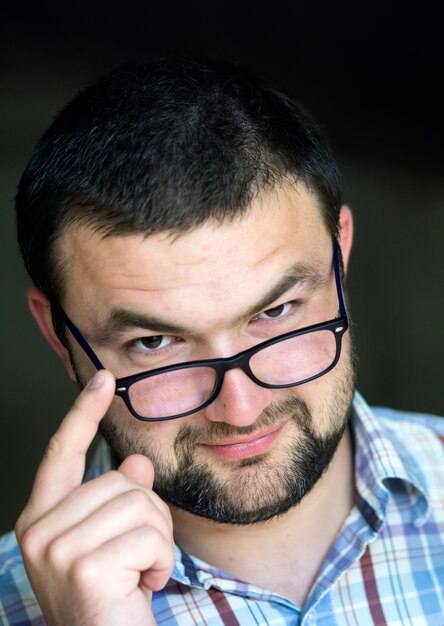 Retrato de bonito barbudo inteligente fotogênico moderno jovem de óculos com corte de cabelo curto e amáveis olhos roxos, sorrindo na câmera no fundo desfocado cinza.