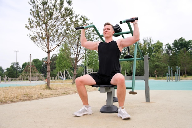 Retrato de bonito feliz homem forte atleta atleta fisiculturista treinando ao ar livre no ginásio ao ar livre no verão ganha músculos de mãos e ombros musculação e fitness estilo de vida saudável