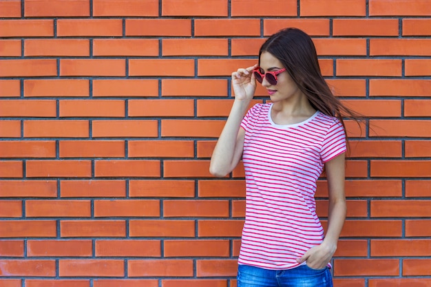 Retrato, de, bonito, menina jovem, em, vermelho, óculos de sol, sobre, parede tijolo vermelho