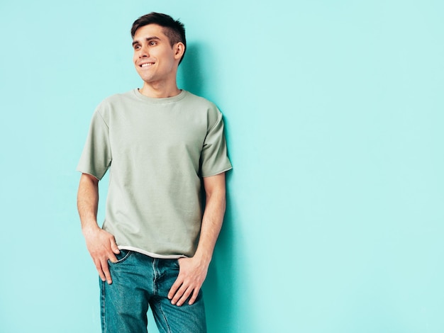 Retrato de bonito sorridente elegante hipster lambersexual modelo Homem vestido de camiseta e jeans Moda masculina isolada no estúdio Posando perto da parede azul Alegre e feliz