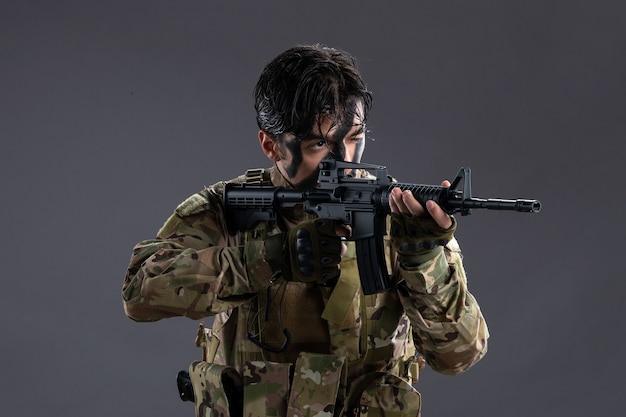 Retrato de bravo soldado em uniforme militar com metralhadora na parede escura