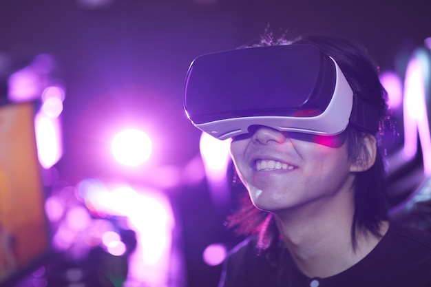 Retrato de cabeça e ombros de jovem asiático usando fone de ouvido VR enquanto joga videogame e sorrindo feliz, copie o espaço