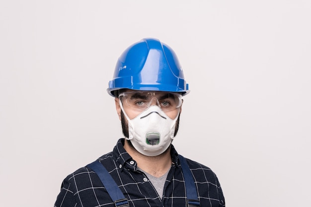 Retrato de cabeça e ombros de um jovem engenheiro ou construtor contemporâneo com capacete e máscara protetora trabalhando em período de quarentena