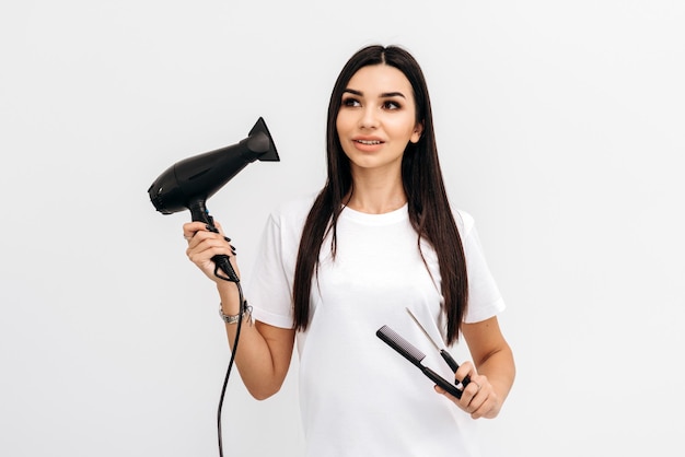 Retrato de cabeleireira morena sorrindo e segurando em seu secador de mãos e pente enquanto posava no estúdio Conceito de estilista profissional