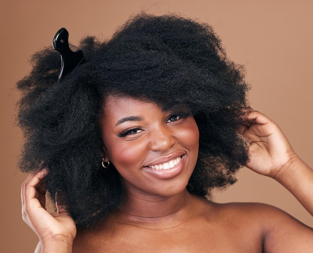 Retrato de cabelo e pente para beleza com uma mulher negra em estúdio em um fundo marrom para cosméticos naturais Sorriso facial e cuidados com os cabelos com uma jovem modelo feminina afro feliz interna para tratamento com shampoo