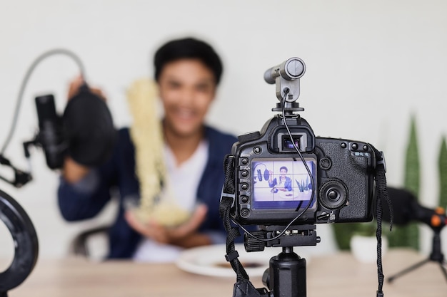 Retrato de câmera filmando vlogging de comida com imagem embaçada de jovem asiático mostrando macarrão.