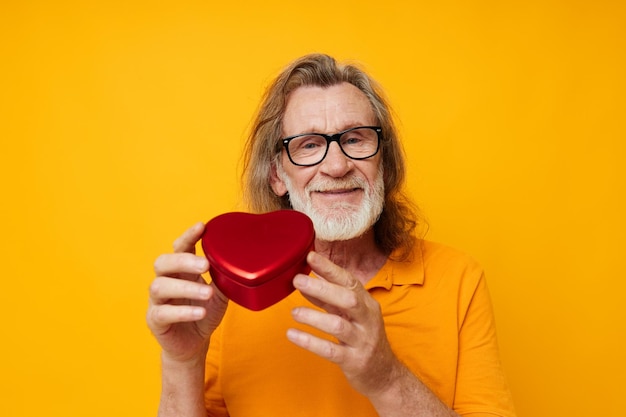 Retrato de camiseta amarela de homem sênior feliz e óculos posando caixa em forma de coração inalterada