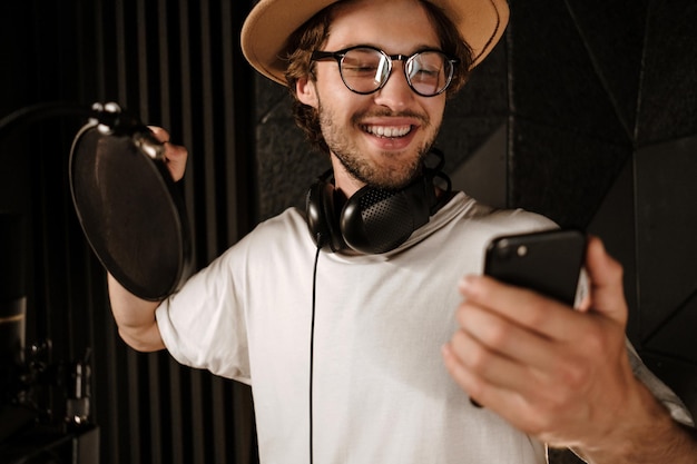 Retrato de cantor masculino elegante bonito com smartphone gravando nova música no estúdio de som moderno