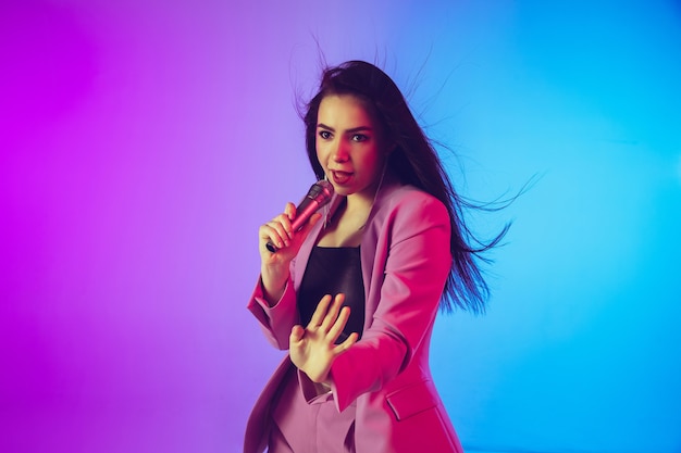 Retrato de cantora caucasiana isolado em fundo gradiente de estúdio em luz de néon
