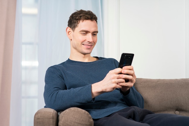 Retrato de cara feliz jovem positivo sorridente usando, olhando para a tela do seu telefone celular.