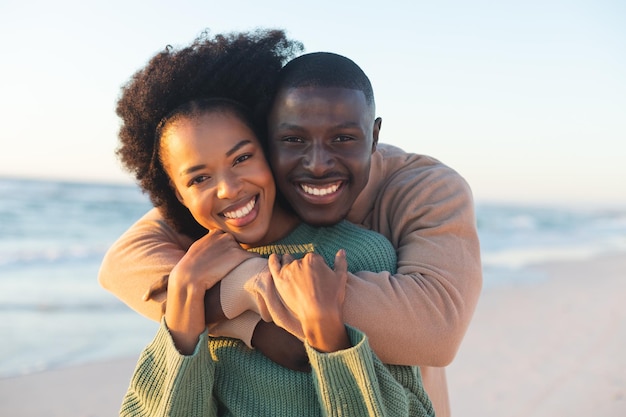 Retrato de casal afro-americano feliz abraçando e sorrindo na praia ensolarada. Verão, união, romance e férias, inalterados.