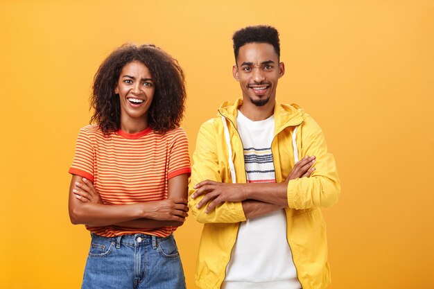 Retrato de casal afro-americano surpreso com penteado afro em pé, cruzando os braços no peito.