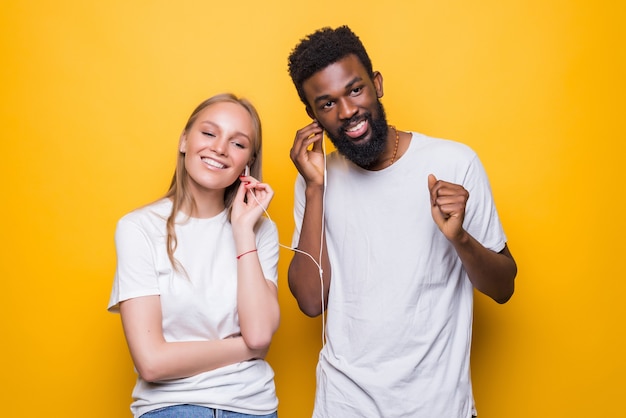 Retrato de casal alegre cantando enquanto usa smartphone e fones de ouvido isolados juntos sobre a parede amarela