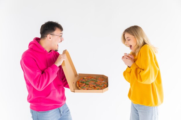 Retrato de casal alegre homem e mulher em suéteres coloridos sorrindo enquanto come pizza