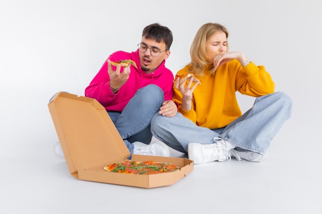 Foto retrato de casal alegre homem e mulher em suéteres coloridos sorrindo enquanto come pizza