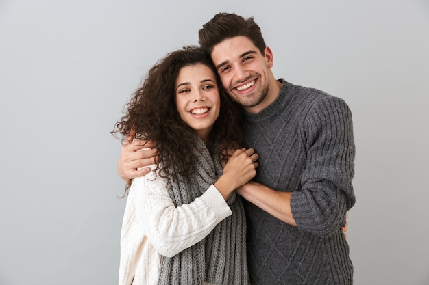 Retrato de casal alegre, homem e mulher, sorrindo enquanto se abraçam, isolado sobre uma parede cinza