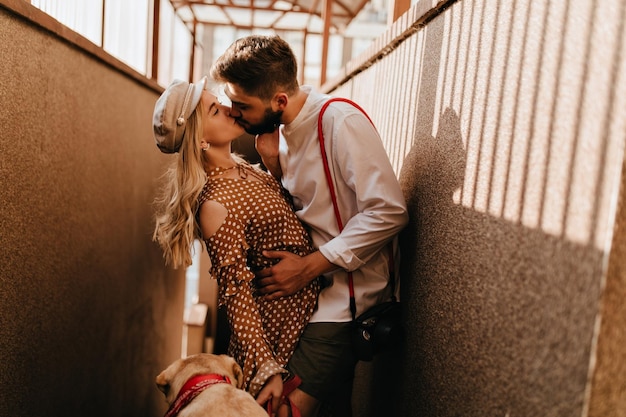 Retrato de casal apaixonado se beijando no corredor garota mantém cachorro na coleira enquanto cara a abraça