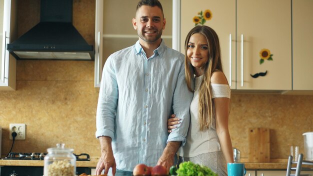 Retrato de casal apaixonado sorrindo ang olhando para a câmera na cozinha em casa