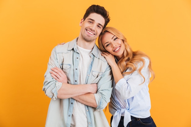 Retrato de casal contente em roupas básicas, sorrindo enquanto uma mulher coloca a cabeça no ombro masculino, isolado sobre a parede amarela