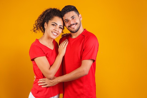 Retrato de casal de conteúdo em roupas básicas sorrindo para a câmera enquanto mulher colocando a cabeça no ombro masculino isolado sobre fundo amarelo ele está surpreso e feliz