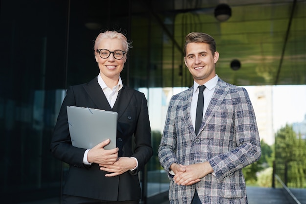 Retrato de casal de empresários bem-sucedidos sorrindo para a câmera enquanto estão juntos ao ar livre